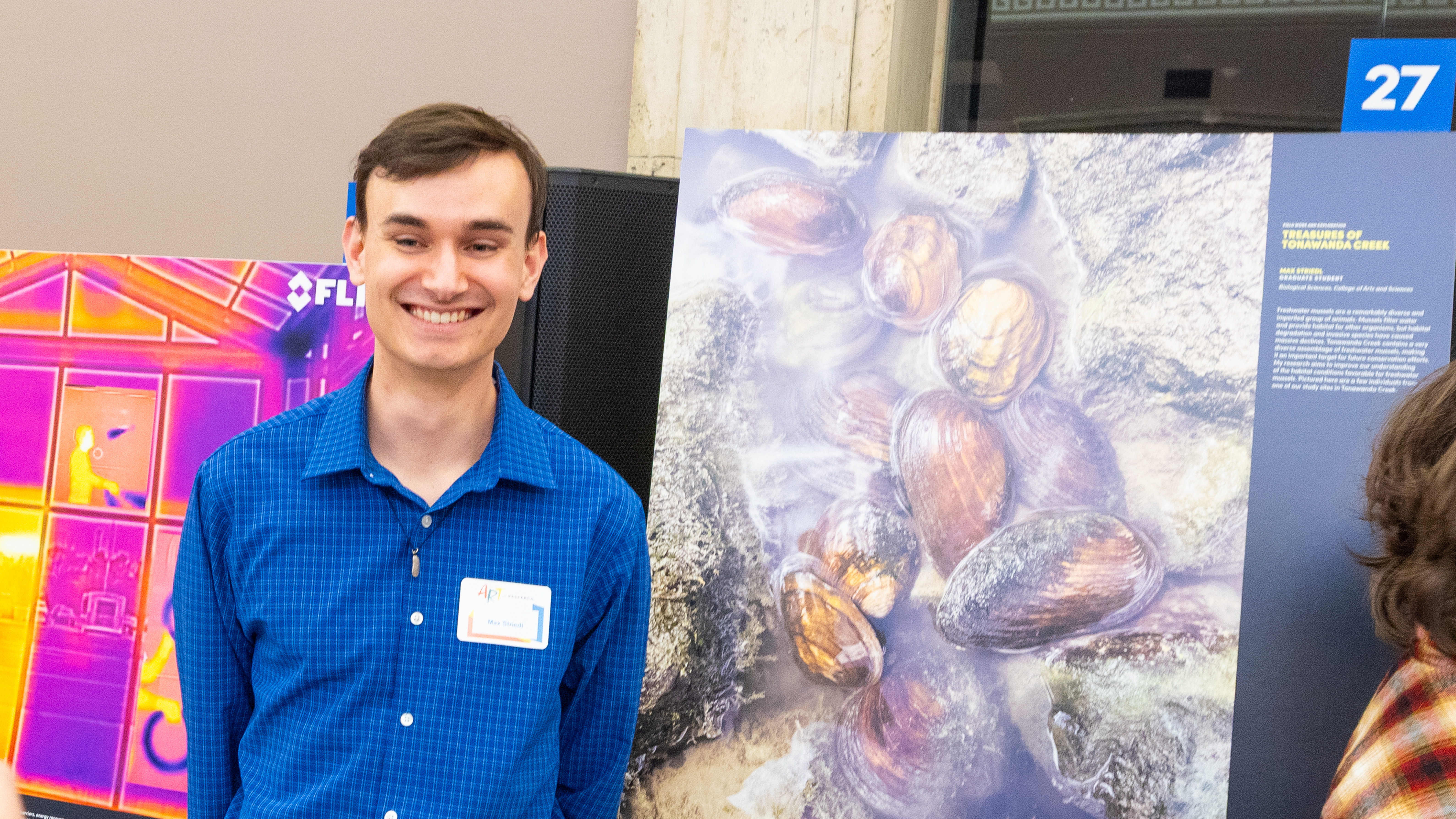 Graduate student stands in front of their Art of Research image submission at the Buffalo Museum of Science during the 2025 Art of Research event.
